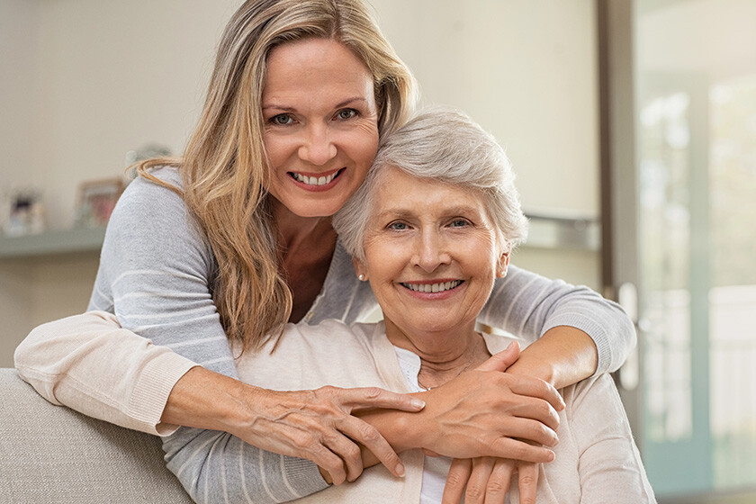 cheerful-mature-woman-embracing-senior-mother-home-looking-camera-portrait